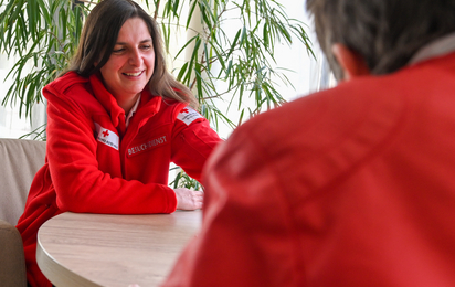 Eine Dame vom Besuchsdienst in roter Uniform plaudert mit ihrer Klientin