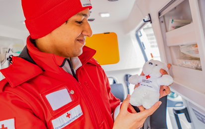 ein Zivildiener ist in einem Rettungsauto und hält den Rotkreuz Teddybären in der Hand