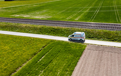 ein fahrendes Rettungsauto aus der Drohnenperspektive fährt über einen Feldweg entlang der Bahnstrecke